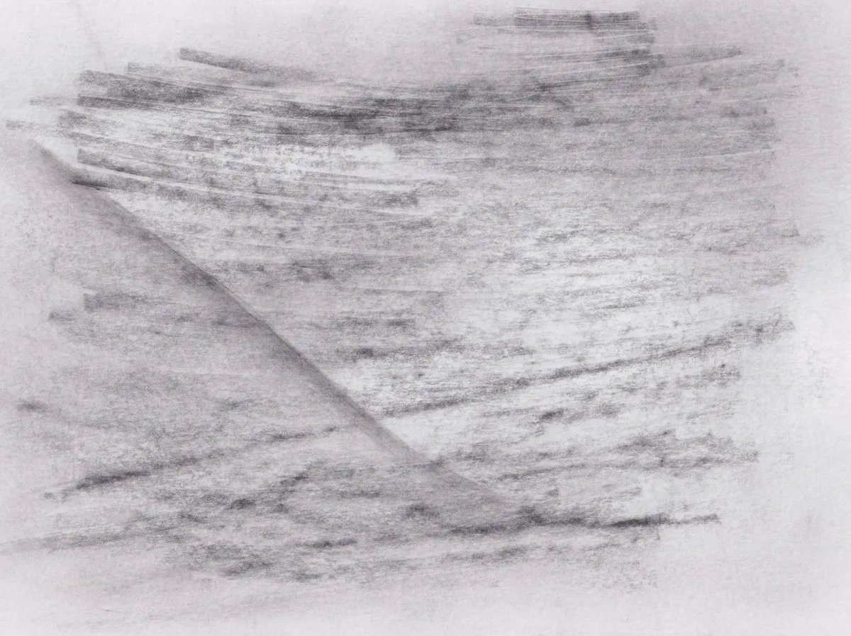 Soft graphite strokes running across white paper, cut by a single diagonal crease of tone