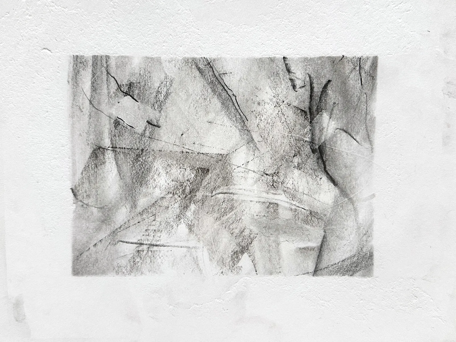 Wide graphite drawing on white paper: overlapping smudged planes crossed by sharp diagonal lines, with dark curved strokes like wings along the right side