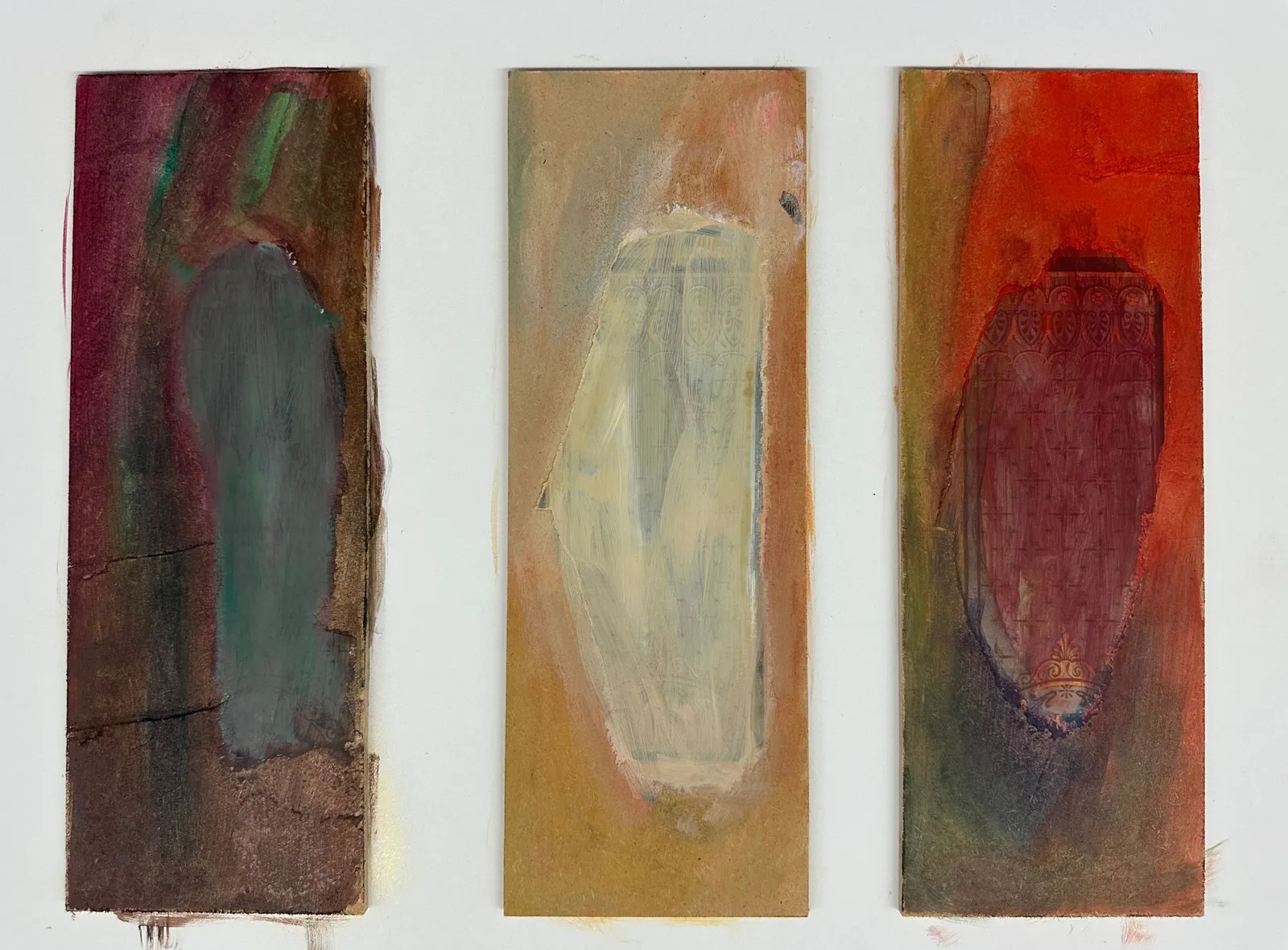 Three narrow upright panels side by side, each holding one soft oval: grey-green on brown, pale cream on ochre, dark red on orange