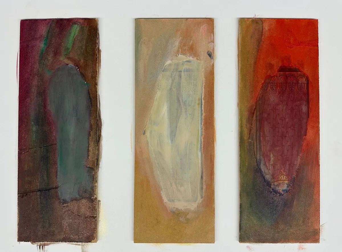 Three narrow upright panels side by side, each holding one soft oval: grey-green on brown, pale cream on ochre, dark red on orange