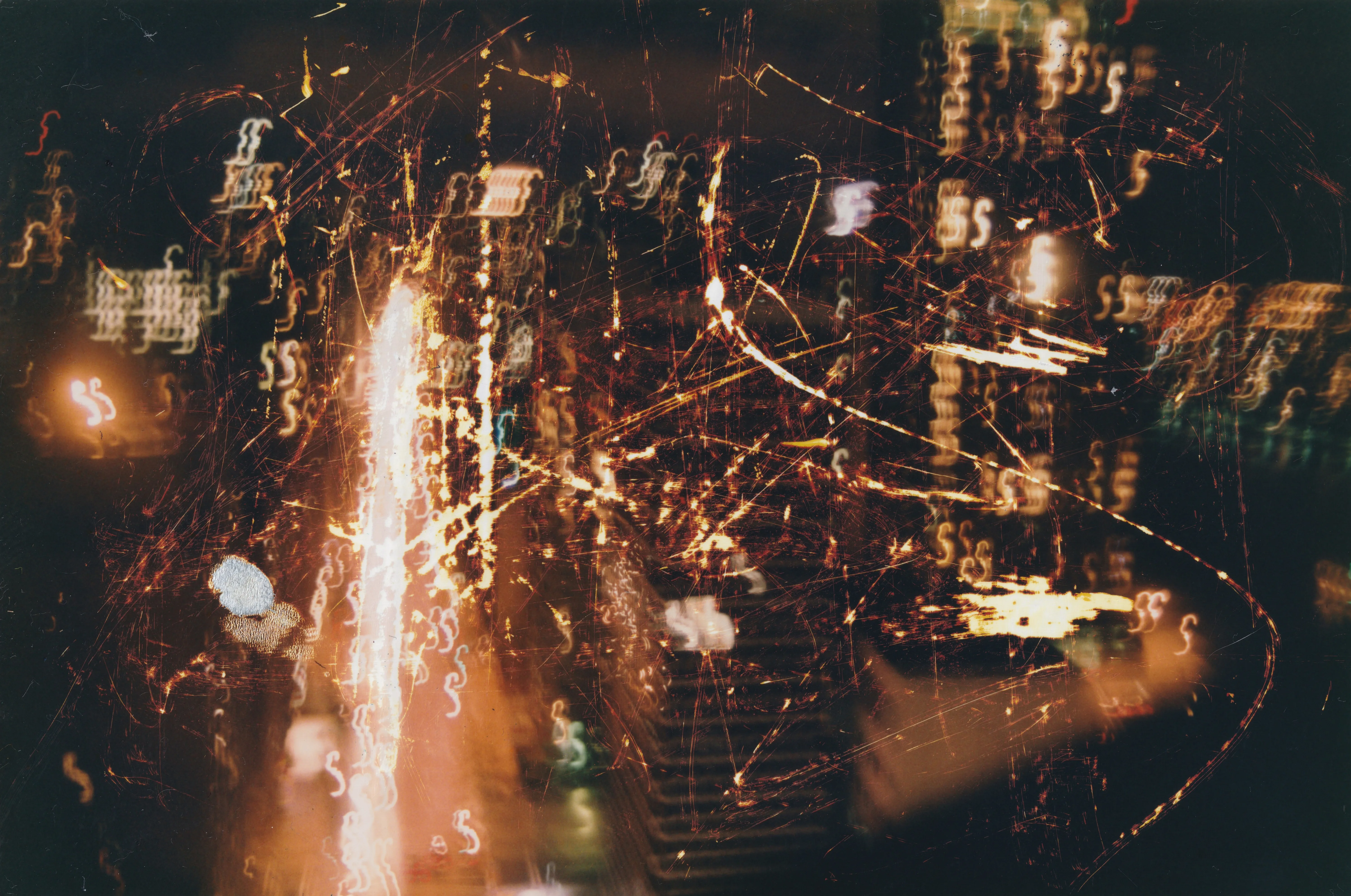Night photograph of city lights blurred into streaks and squiggles, scratched with fine orange lines